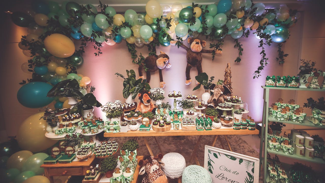 Beautifully arranged jungle-themed dessert table with balloons and plushies indoors.