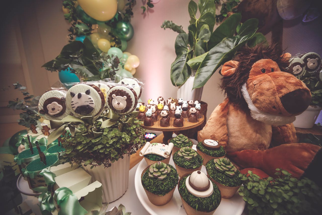 A vibrant jungle themed dessert table featuring animal cupcakes and plush toys.